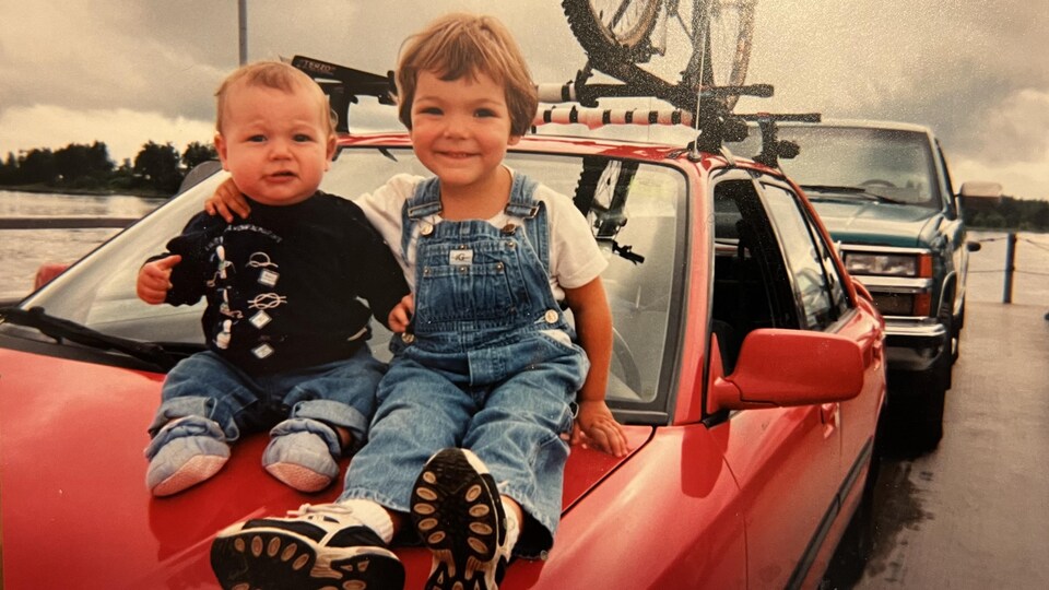 Deux jeunes enfants sont pris en photo sur le capot d'une voiture.