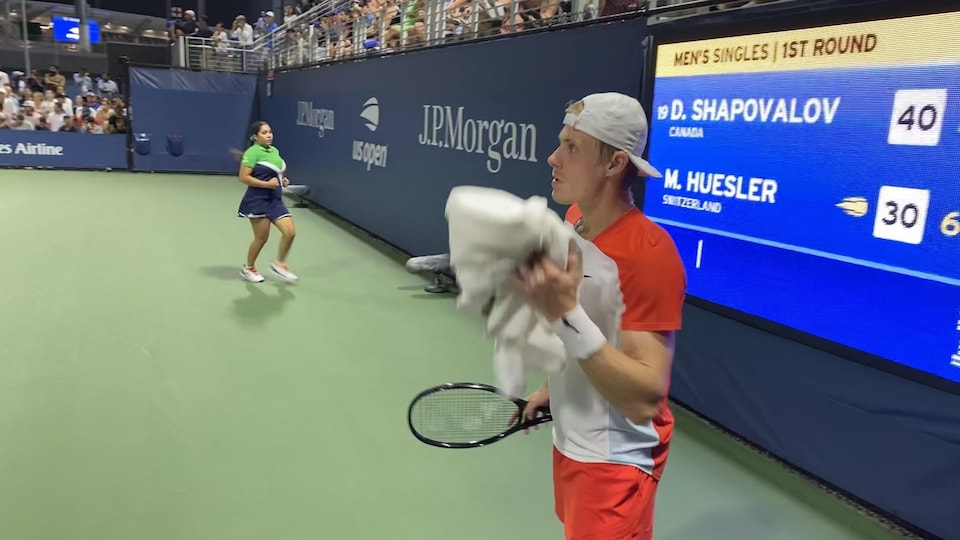 A tennis player takes his towel to wipe between two points. 