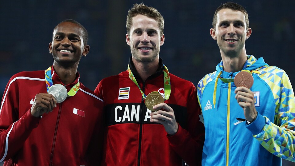 Il montre sa médaille avec les autres sur le podium.