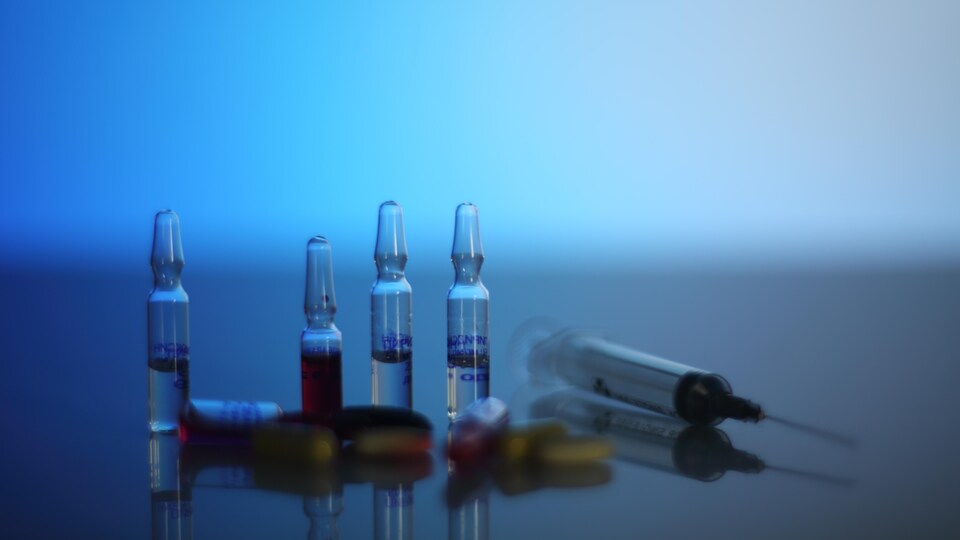 Sur une table, quatre ampoules avec du liquide à l'intérieur, une seringue et des pilules.