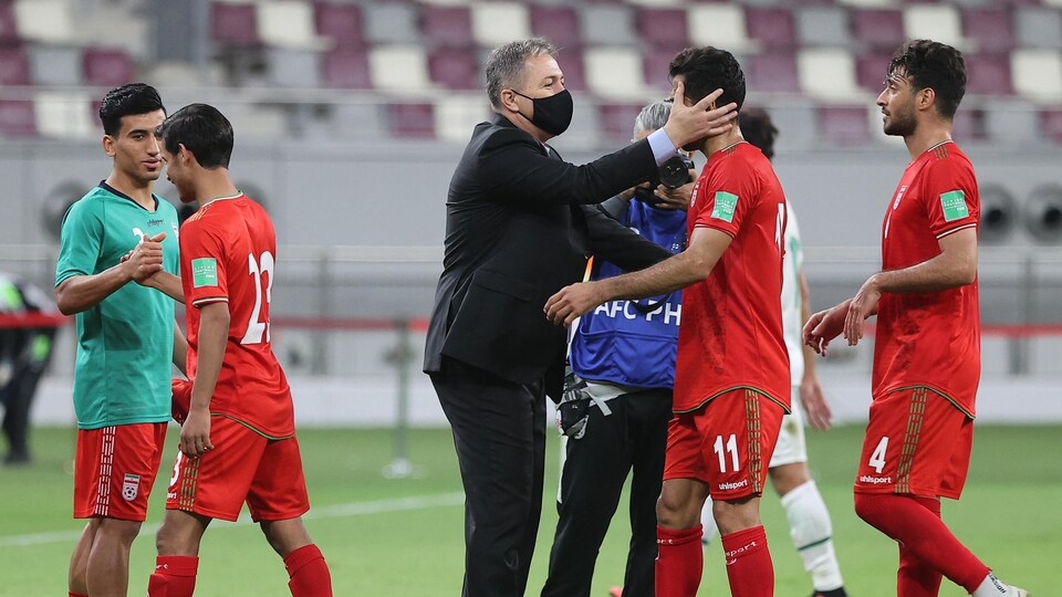 Un homme en veston félicite des joueurs de soccer.