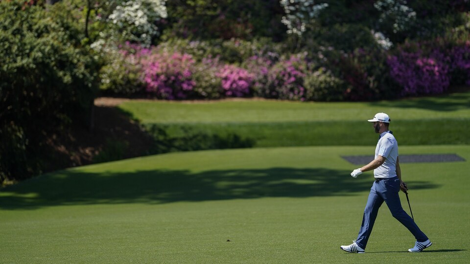 Un golfeur marche sur un terrain bordé de fleurs.