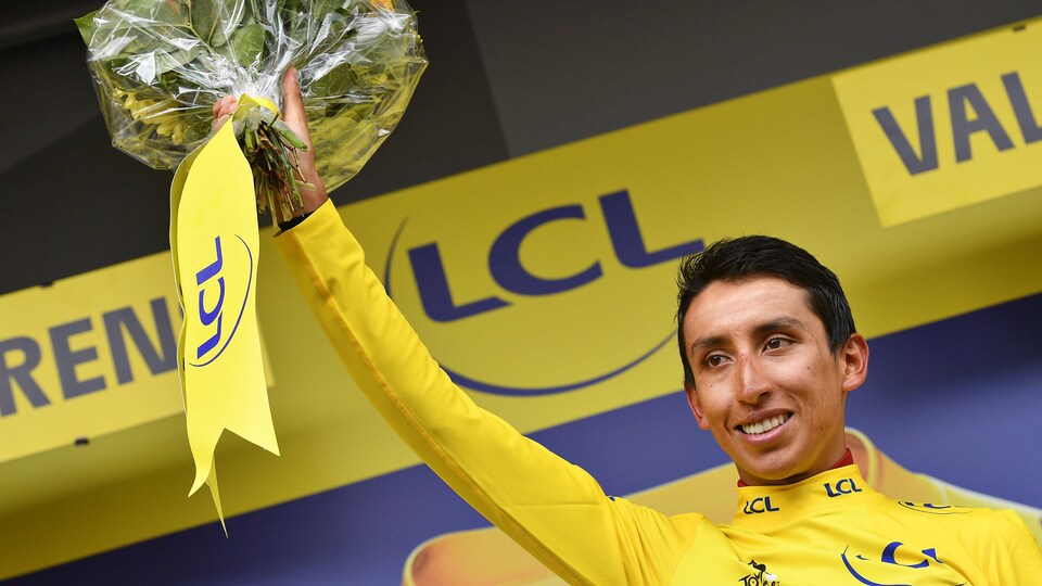Il endosse le maillot jaune sur le podium et tient à bout de bras un bouquet de fleurs.
