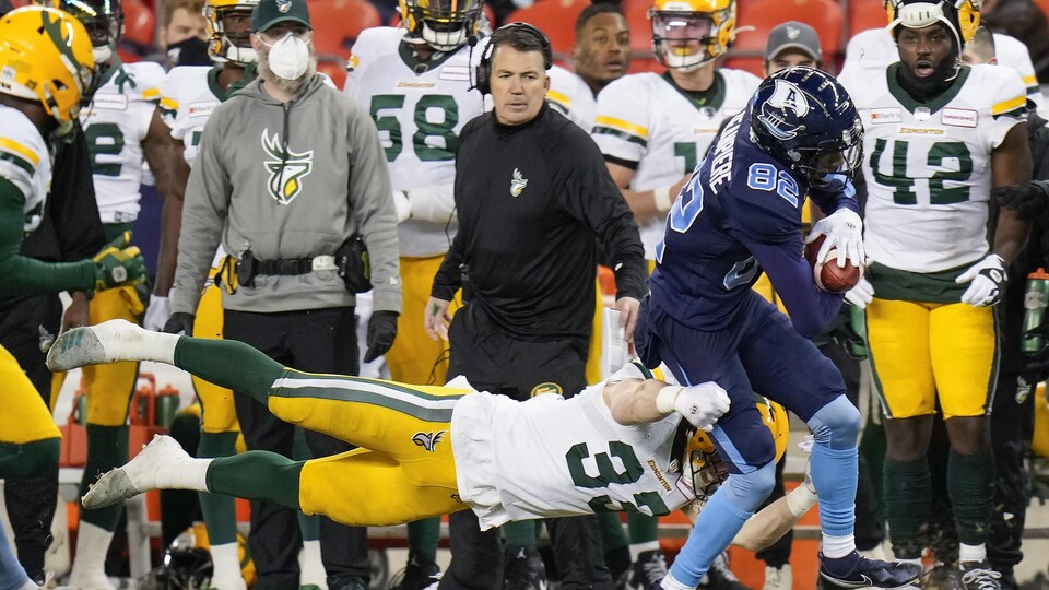 Le receveur des Argonauts de Toronto, Cam Phillips, se fait plaquer devant l'entraîneur-chef des Elks, Jamie Elizondo, et quelques joueurs sur les lignes de côté.