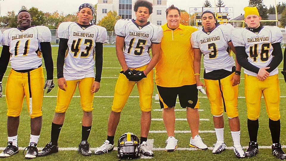 Des joueurs de football d'une école secondaire, vêtus de blanc, jaune et noir, prennent la pose avec leur entraîneur. 