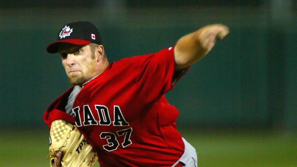 Homme avec uniforme de baseball du Canada, vient de lancer une balle en grimaçant.