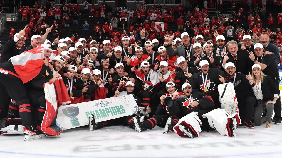 Un groupe de joueurs et d'entraîneurs célèbrent leur victoire d'une médaille d'or au centre de la glace.