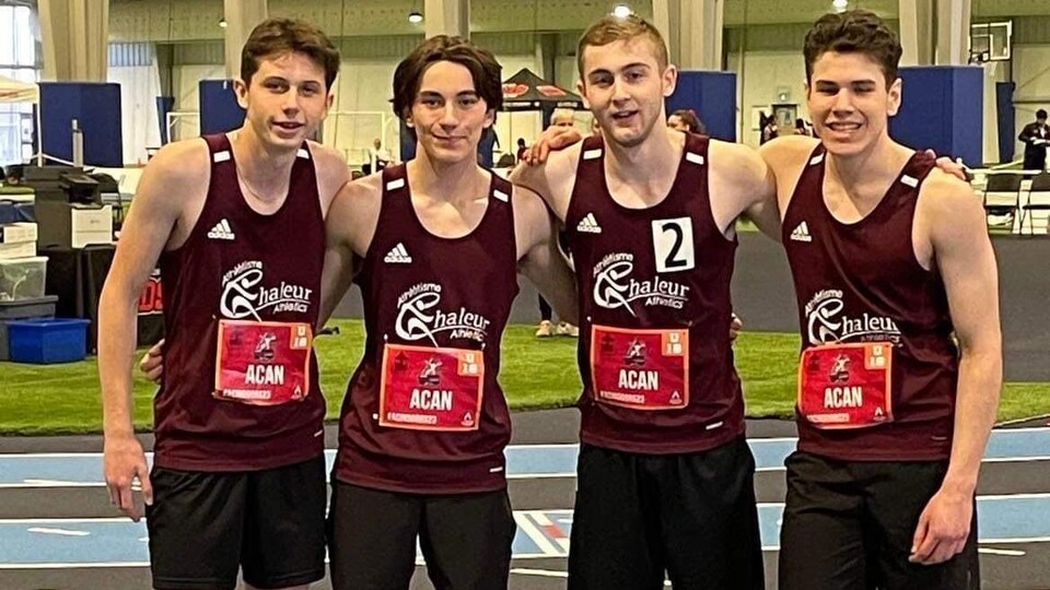 Quatre coureurs portant les uniformes de course sur la piste avec les installations en arrière-plan.