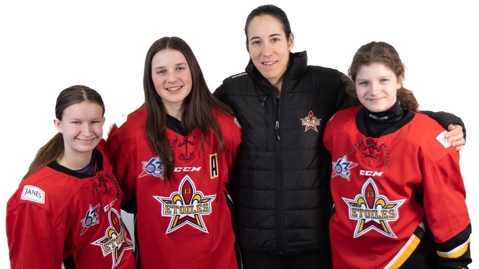 Trois joueuses de hockey avec le nom de leur équipe, les étoiles, sur leur chandail, prennent une photo avec une ancienne membre de l'équipe nationale du Canada.