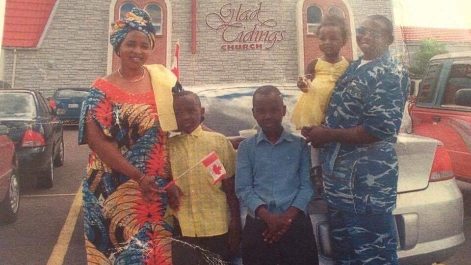 La mère a un main sur l'épaule d'Héritier, le père tient sa fille dans ses bras. Les parents portent leurs vêtements traditionnels africains. Les enfants sont habillés comme de jeunes nord-américains. Ils sont devant une église.