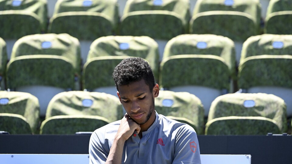 Un joueur de tennis, vêtu de gris, est assis, songeur, devant des sièges vides après une finale perdue.