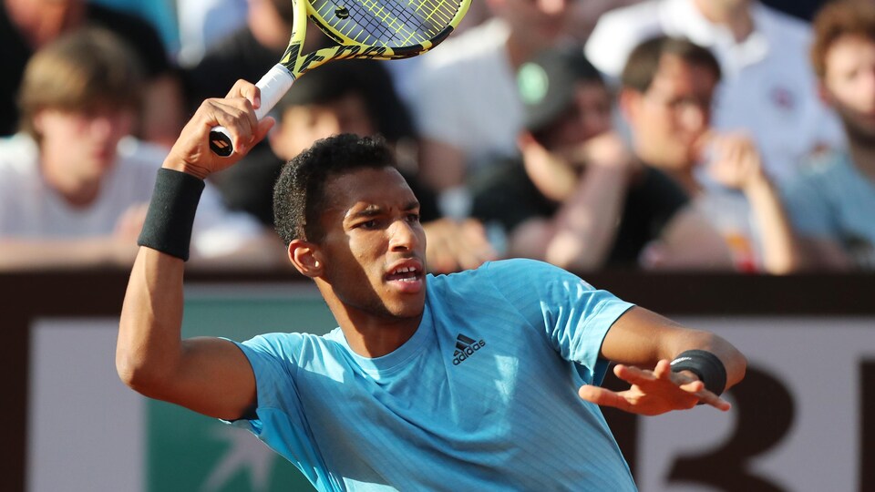 A player hits his forehand ball (right hand) and watches it. The spectators in the background are watching.