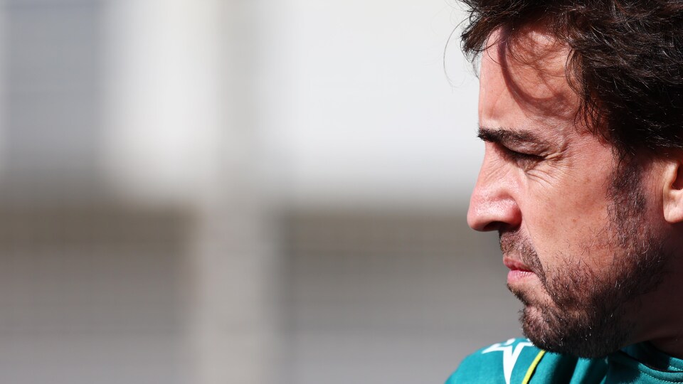 Un pilote de F1, de profil, regarde au loin.