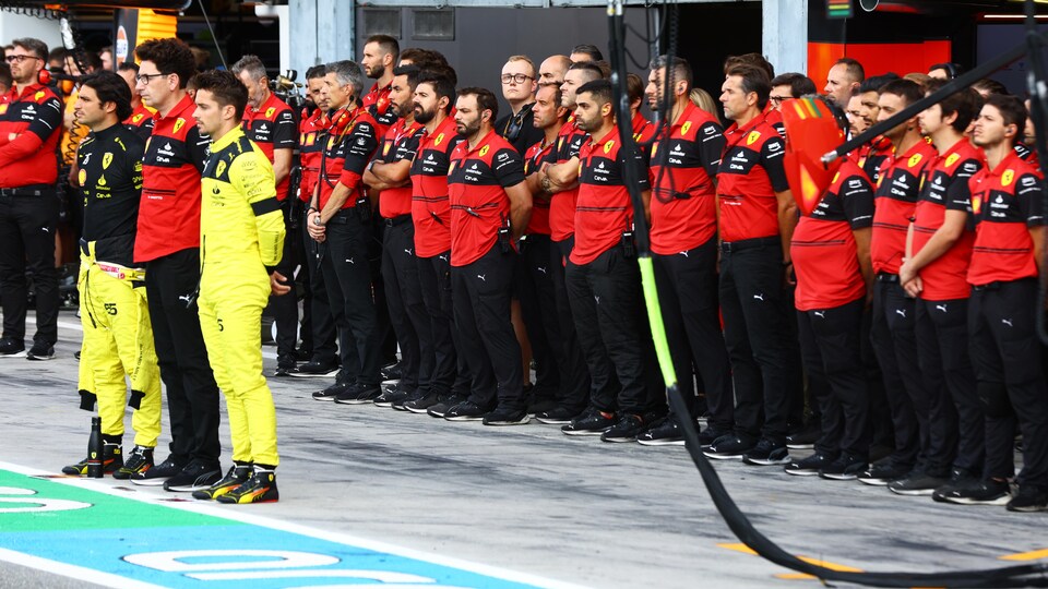 The Ferrari team staff are lined up in the pits, gathered for a minute's silence.