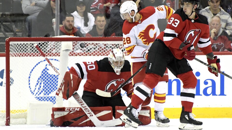 Le centre des Flames Elias Lindholm fait dévier la rondelle dans le filet des Devils, derrière Nico Daws, alors que le défenseur Ryan Graves n'y peut rien.