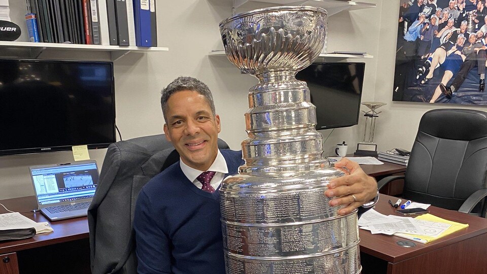 Homme assis dans un bureau et tenant un trophée, la coupe Stanley.