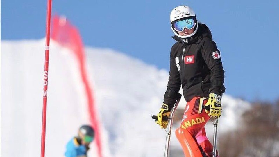 Une skieuse à l'arrêt sur un parcours tient ses stabilisateurs dans chaque main et regarde sur sa gauche vers le bas de la pente.