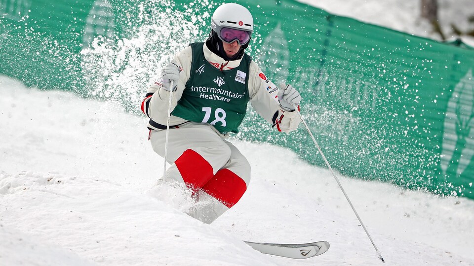 De la neige s'élève derrière les skis du bosseur.