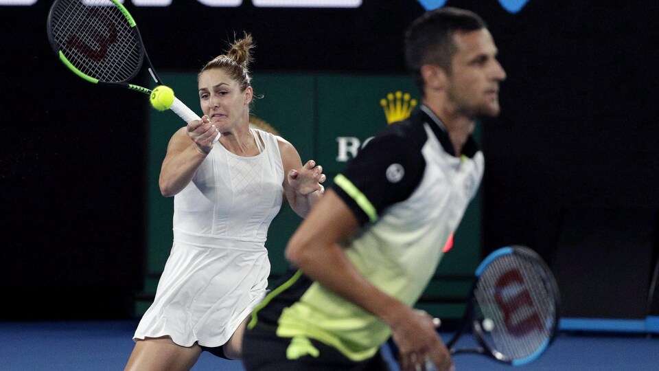 Une jeune femme fait une grimace en frappant la balle pendant un match de tennis double mixte.