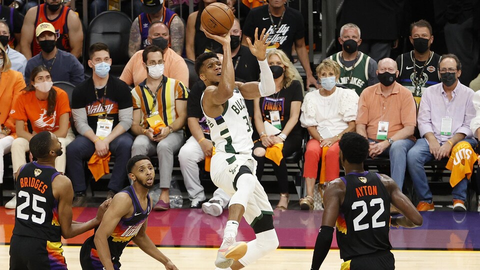 Entouré de trois joueurs adverses, Giannis Antetokounmpo saute pour effectuer un tir au panier.