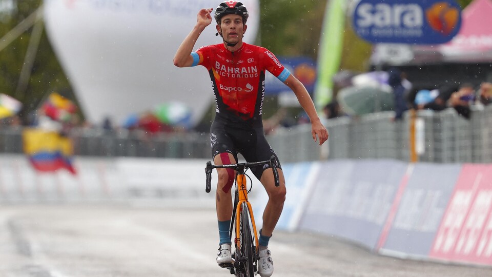 Le cycliste lève le bras droit dans les airs en franchissant la ligne d'arrivée sous la pluie.
