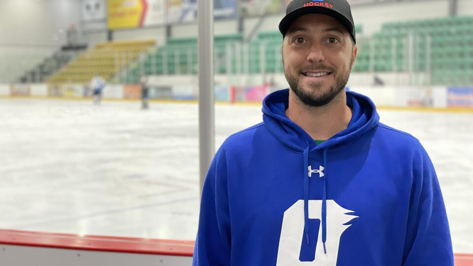 Un entraîneur de hockey prend la pose pour la caméra près d'une patinoire.