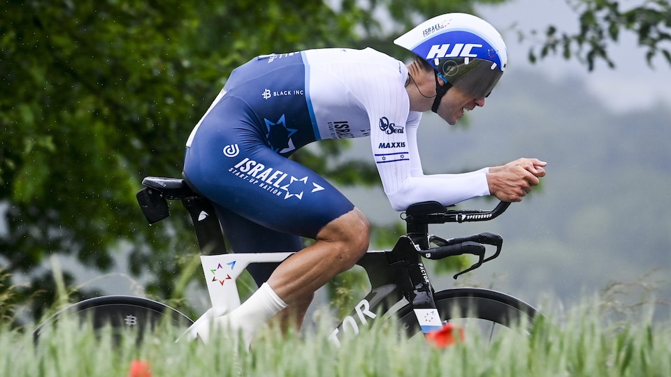 Le cycliste en position aérodynamique avec de l'herbe et des fleurs en avant-plan.