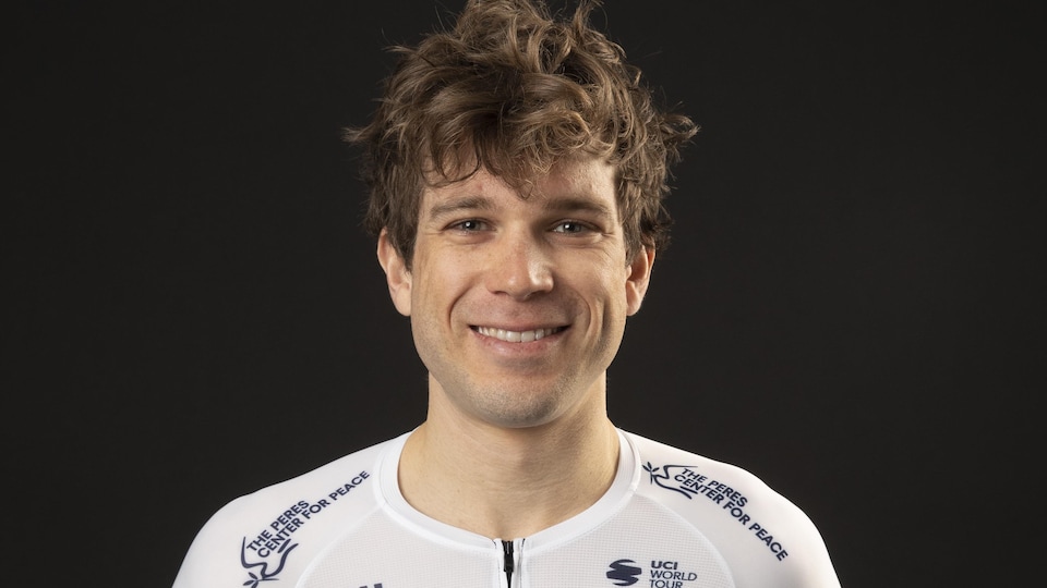 Il regarde la caméra en souriant.