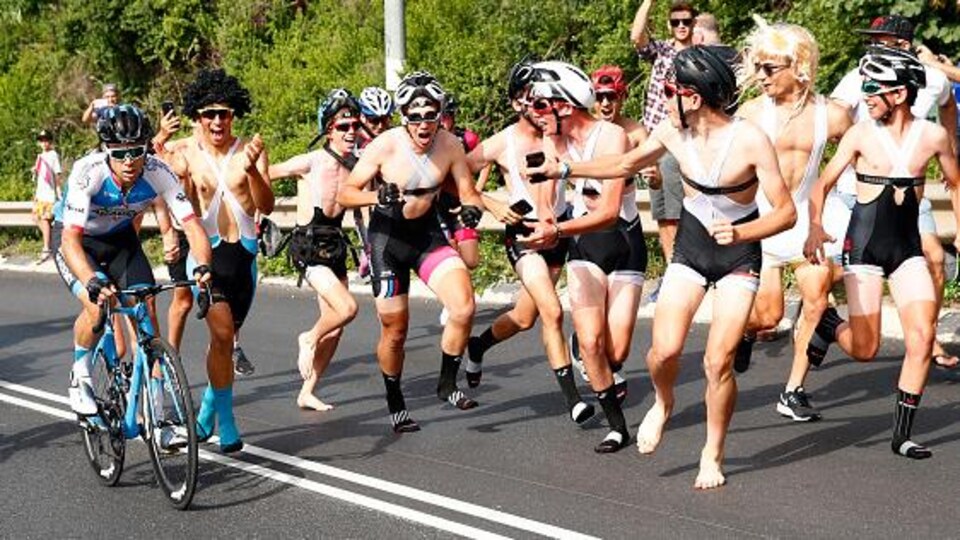 Un cycliste monte une pente entouré d'amateurs de vélo.