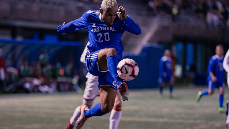 Dans les airs, un joueur de soccer frappe un ballon du pied droit.