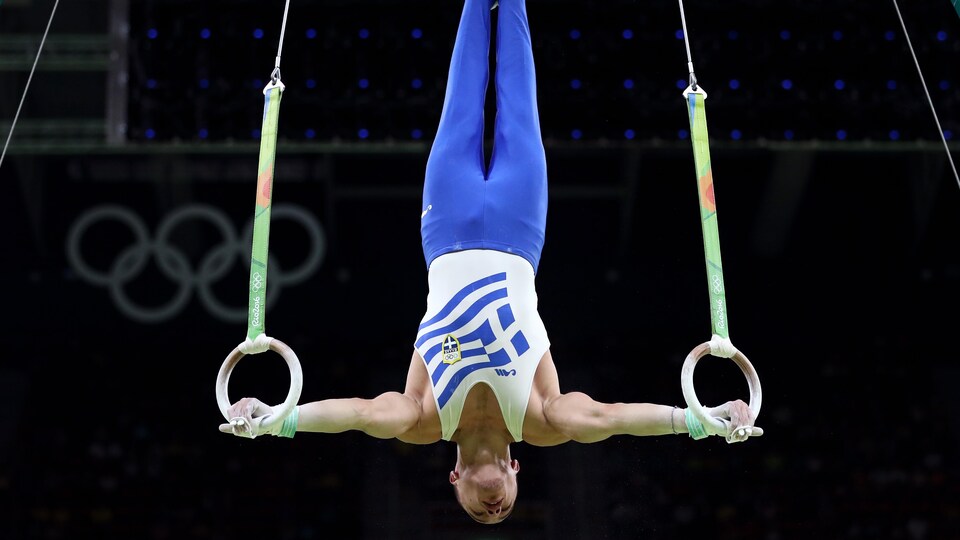 Le gymnaste tient les anneaux.