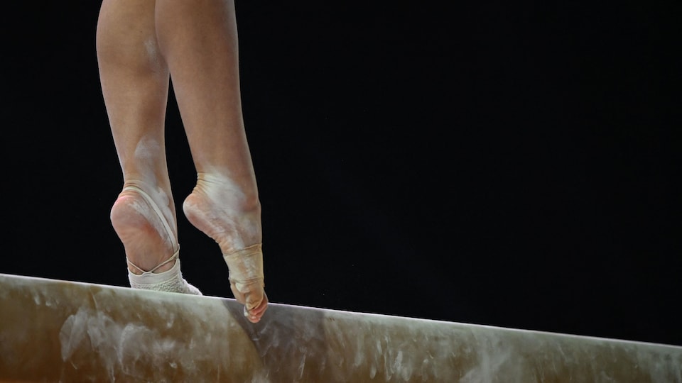 On voit les jambes d'une gymnaste qui participe à une épreuve à la poutre.