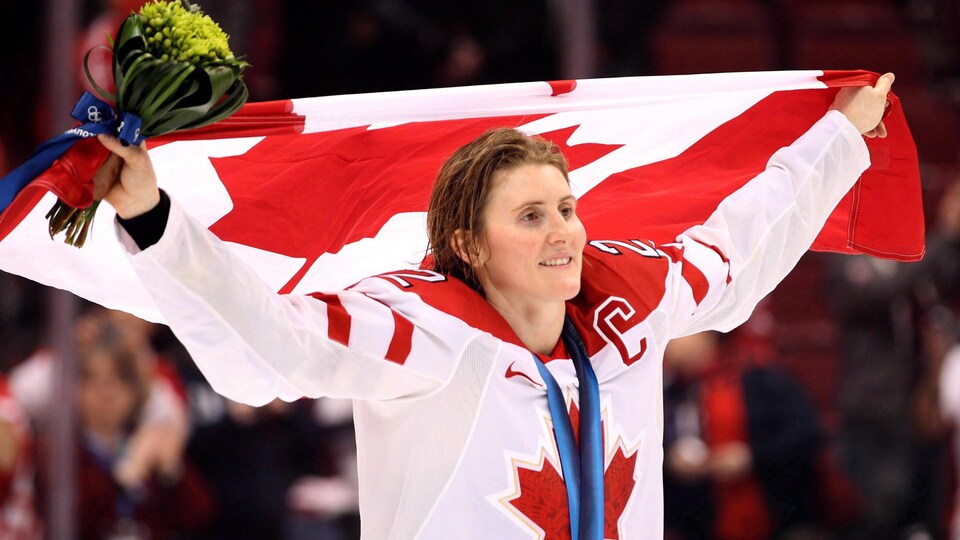 Hayley Wickenheiser avec sa médaille d'or olympique et le drapeau canadien au-dessus de la tête sur la patinoire à Vancouver