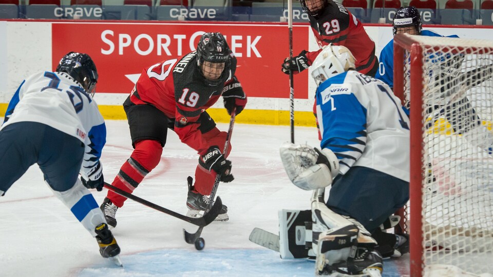 Une joueuse canadienne portant le numéro 19 tirant dans les buts face à deux Finlandaises. 