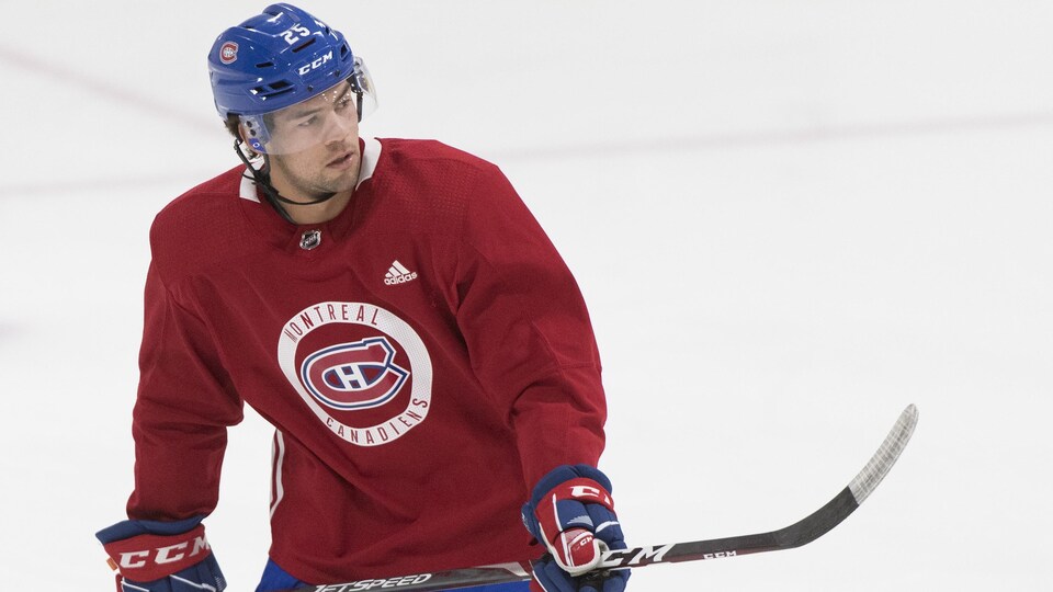 Un joueur de hockey regarde à sa gauche et tient son bâton à deux mains sur la glace.