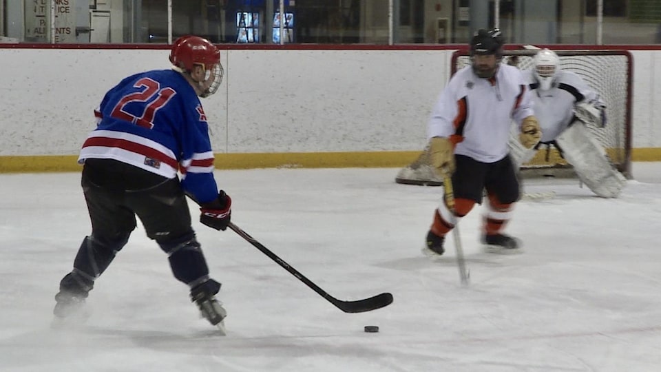 Un joueur de hockey mineur fait face à un autre joueur et au gardien, sur la glace.
