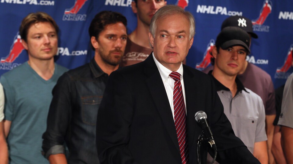 Un homme en veston parle au micro devant des joueurs de hockey.