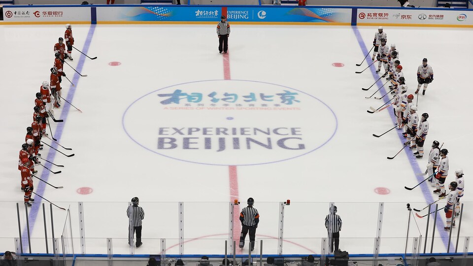 Deux équipes de hockey, en rang à leur ligne bleue, se font face.