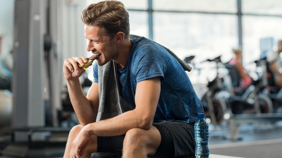 Un homme mange une barre tendre dans une salle d'entraînement.