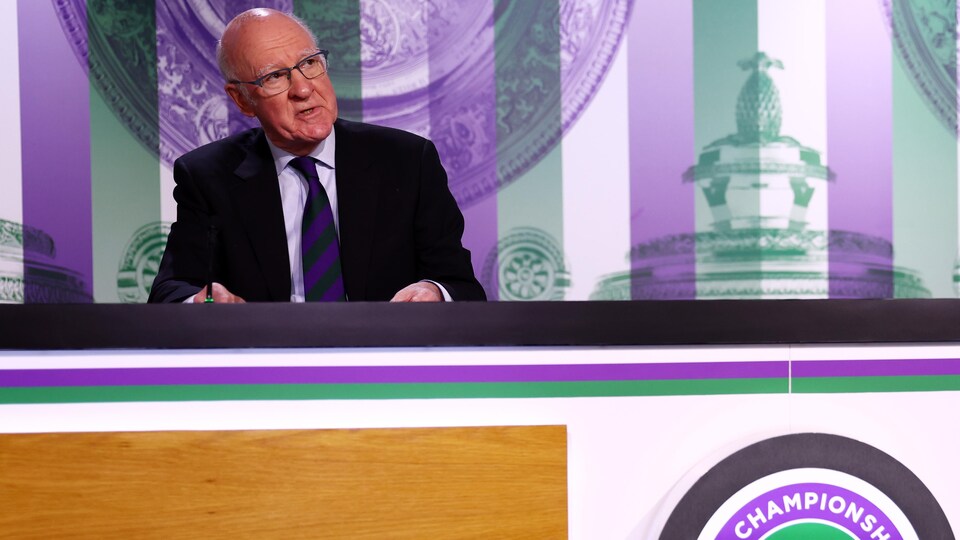 Un homme parle derrière une table avec le logo du tournoi de Wimbledon.