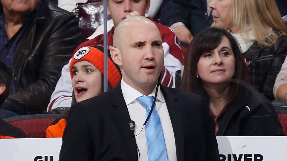 L'ancien joueur de hockey, vêtu d'un complet, observe l'action, debout derrière le banc des Flyers, pendant un match en 2014 en Arizona.