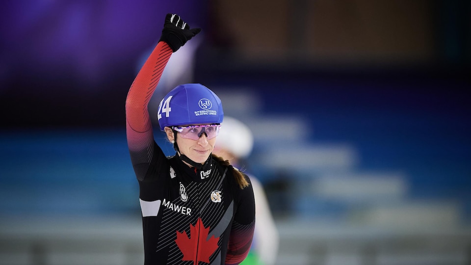 Ivanie Blondin lève le bras dans les airs et salue la foule avec un sourire.