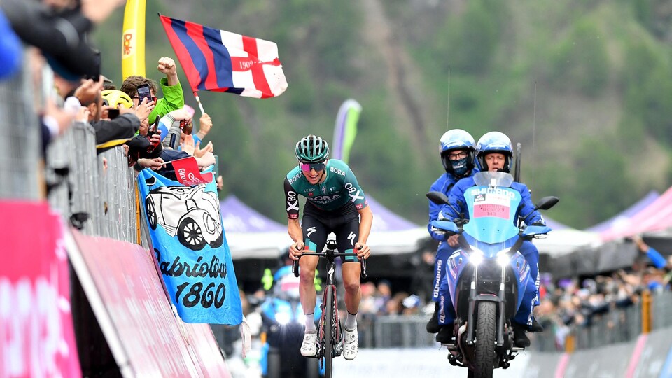 Accompanied by a motorcyclist, he pedaled to reach the finish line. 