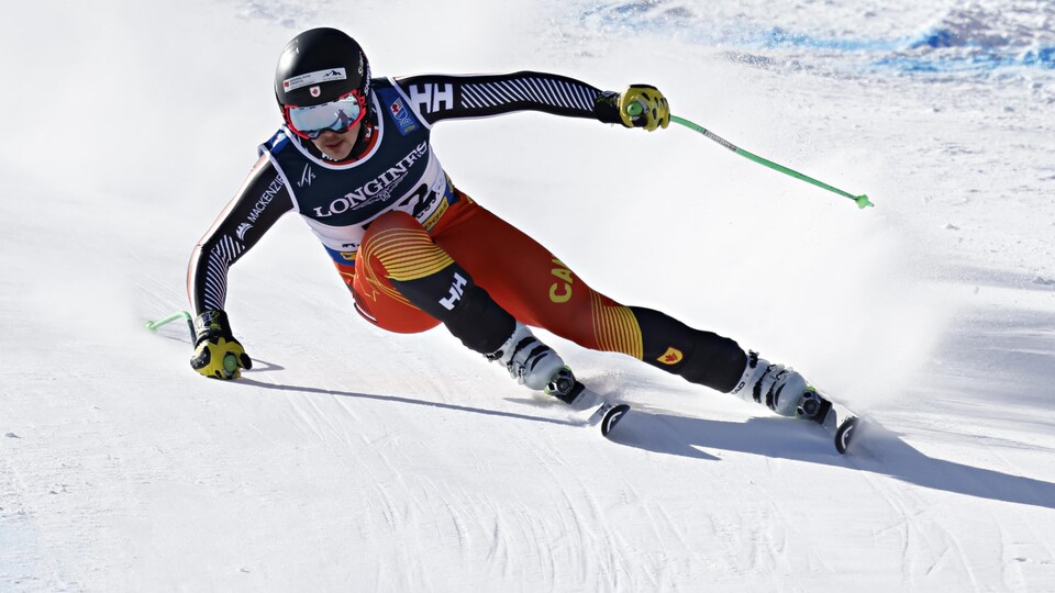 Un skieur dévale une pente et négocie un virage à droite, la main droite sur la neige pour garder son équilibre.  