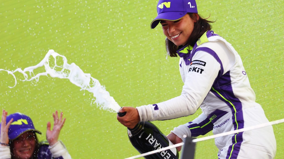 Jamie Chadwick souriante asperge la foule de mousseux sur le podium du GP d'Autriche.