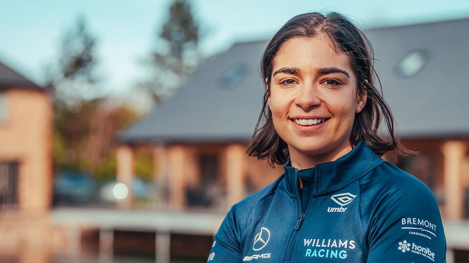 Une jeune femme regarde la caméra et sourit, les bras croisés, dans l'uniforme d'une équipe de F1.
