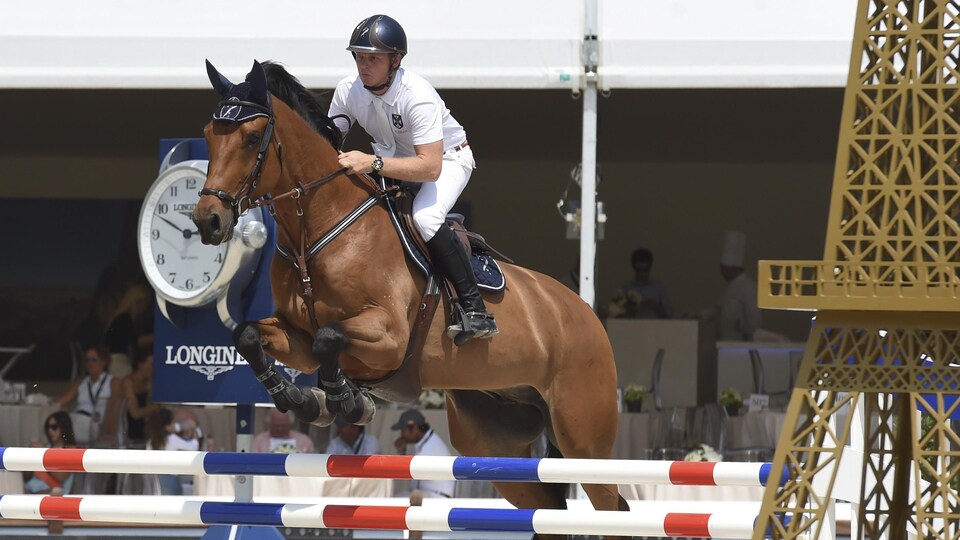 Un cavalier en blanc sur son cheval qui franchit un obstacle.