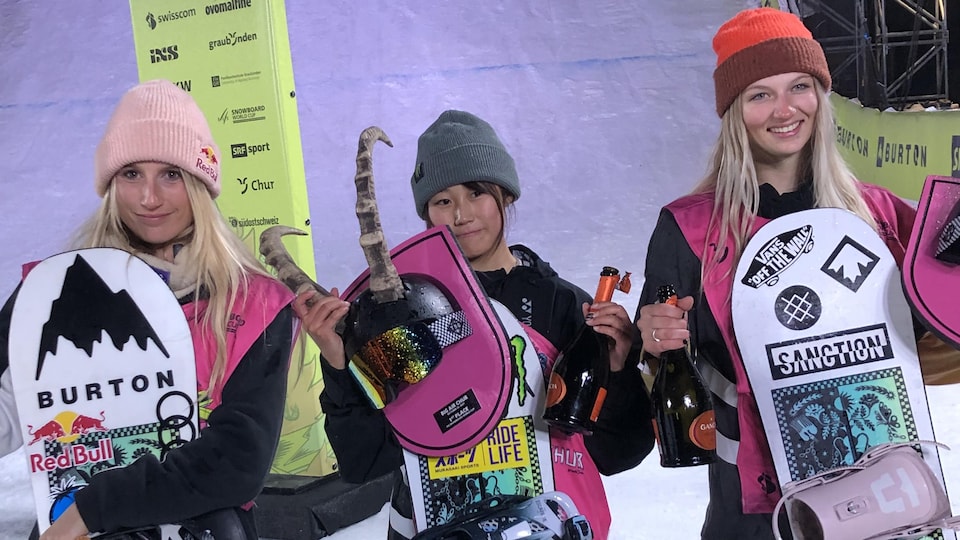les trois gagnantes devant la pente du grand saut, trophées et bouteille de champagne en main.