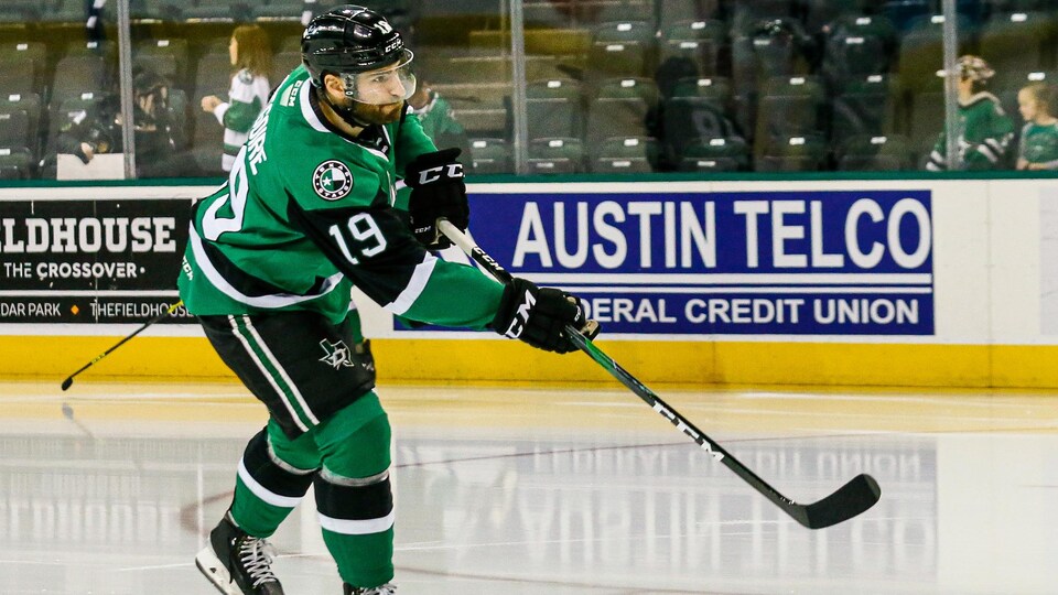 A hockey player, wearing a green, black and white uniform, threw a puck during a warm-up before a game. 