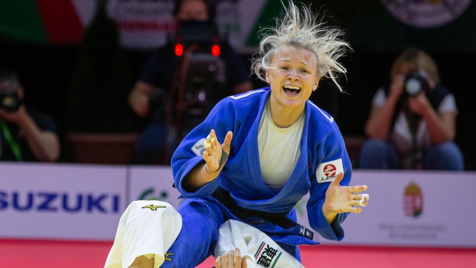 L'athlète lève la tête et sourit à pleines dents, les cheveux en l'air, son adversaire au sol, battue.